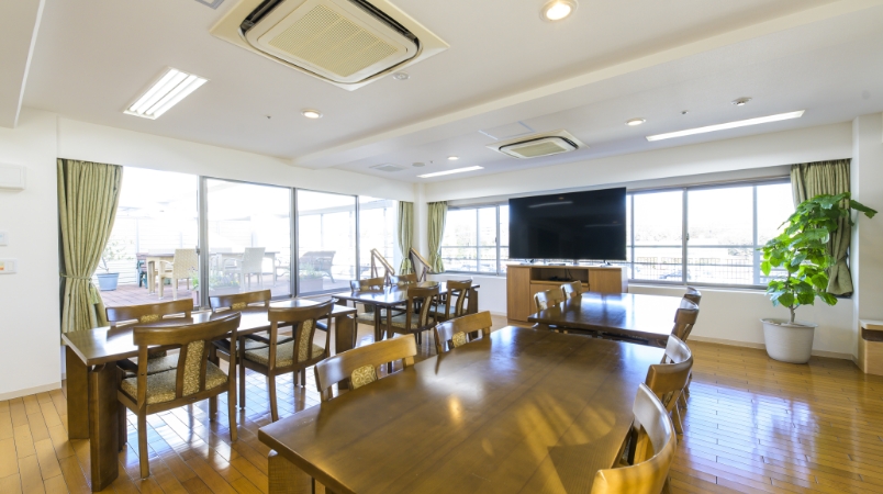 大きな窓からの眺望が特徴の共用リビング。テレビ、テーブル、植栽などで居心地の良い空間。