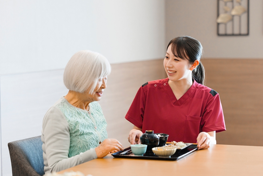 スタッフが入居者に食事をサービスしている様子。温かいおもてなしが感じられる。