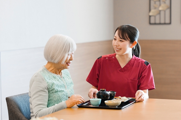 介護職員が入居者に食事をサポートする様子。笑顔で対応している。