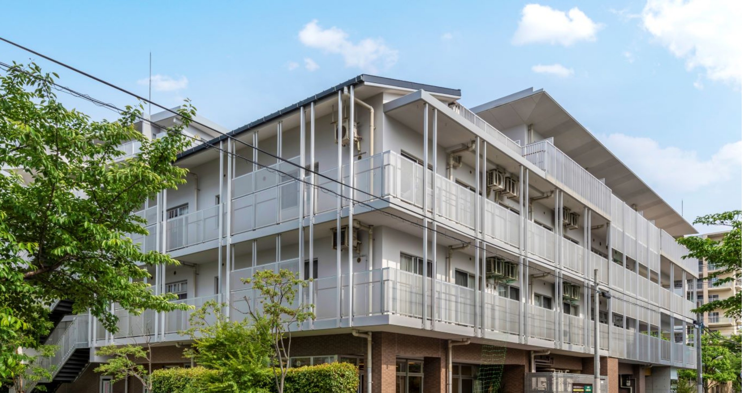 複数階建ての介護施設の建物外観。白とベージュの色合い、バルコニー付きの明るい外観