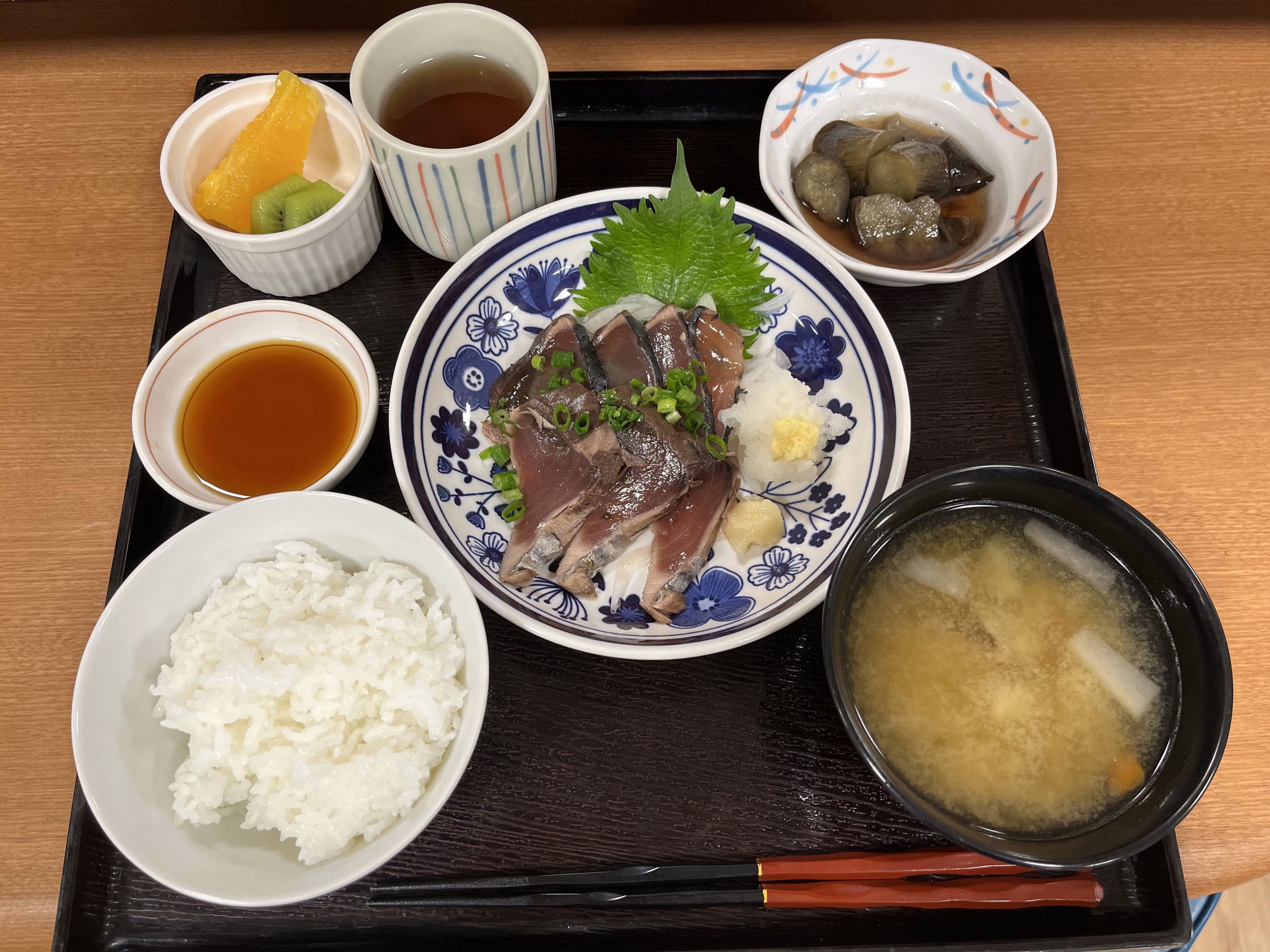 介護施設の食事トレー。白米、刺身、味噌汁、漬物、デザート、飲料が盛られている。